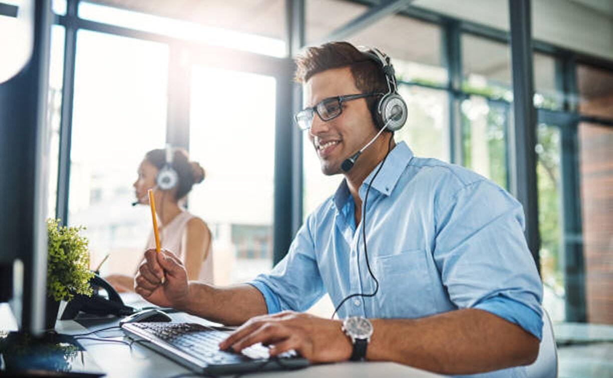 A man wearing headphones and a headset is engaged in tasks on his computer.